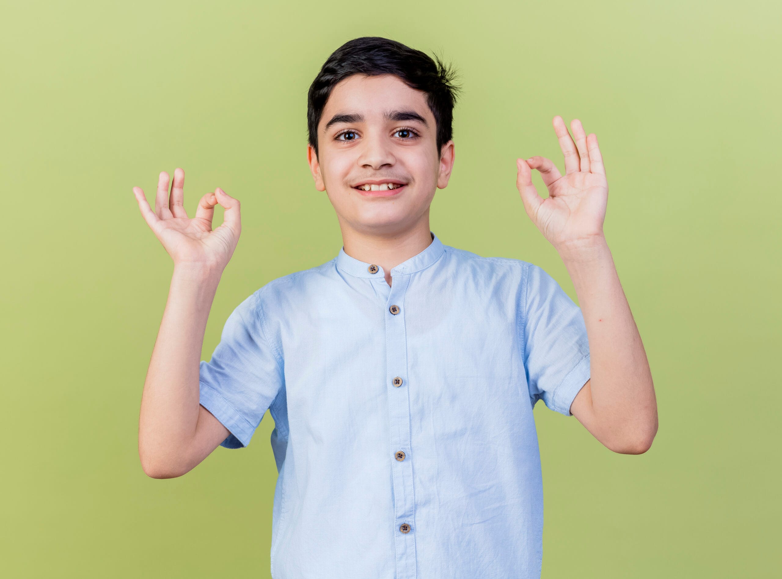 smiling young caucasian boy looking at camera doing ok sign isolated on olive green background